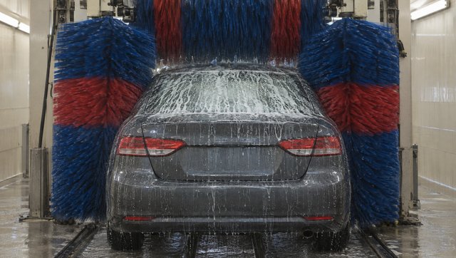 A grey sedan inside a car wash, the brushes closing over it