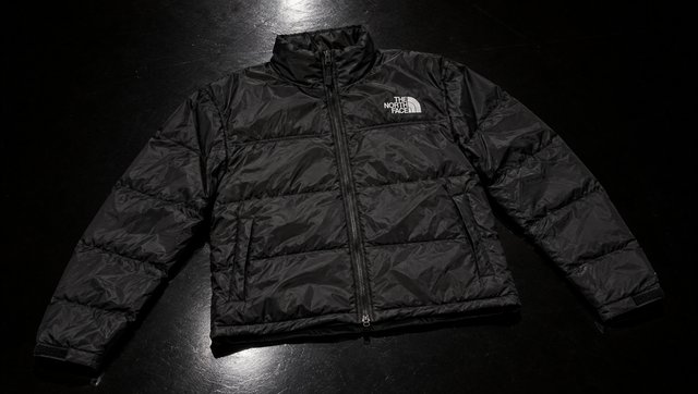 The Nuptse jacket flat and empty on a black floor