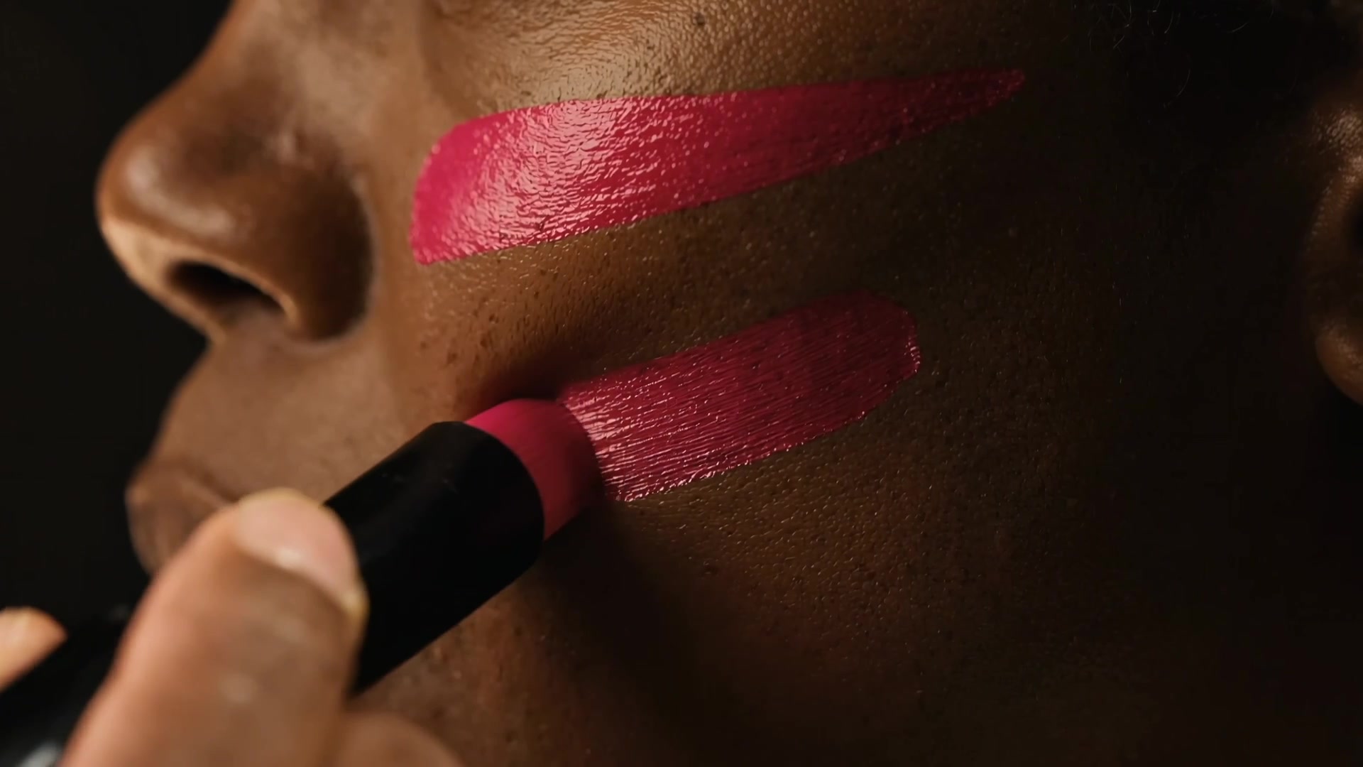 Two magenta stripes of game-day face paint drawn down a cheek in close-up, from the hero spot