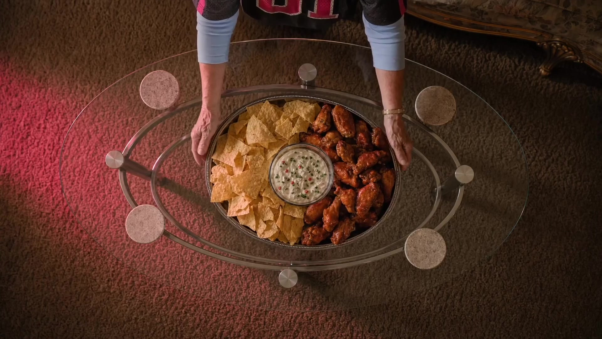 Overhead of the game-day spread set down on the glass table: chips, wings and dip on a silver tray, from the hero spot